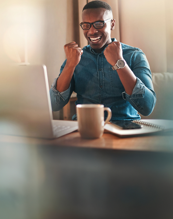 Imagem de um homem preto vestindo camisa azul que está em sua mesa conferindo uma mensagem no computador. Ele está feliz e comemorando por ter sido sorteado.