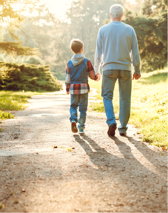 Imagem de pai e filho caminhando de mãos dadas e de costas. O pai é branco e usa um casaco azul e o filho é pequeno de pele branca, cabelos loiros e usa um casaco colorido. O pai está passando proteção e segurança ao filho.