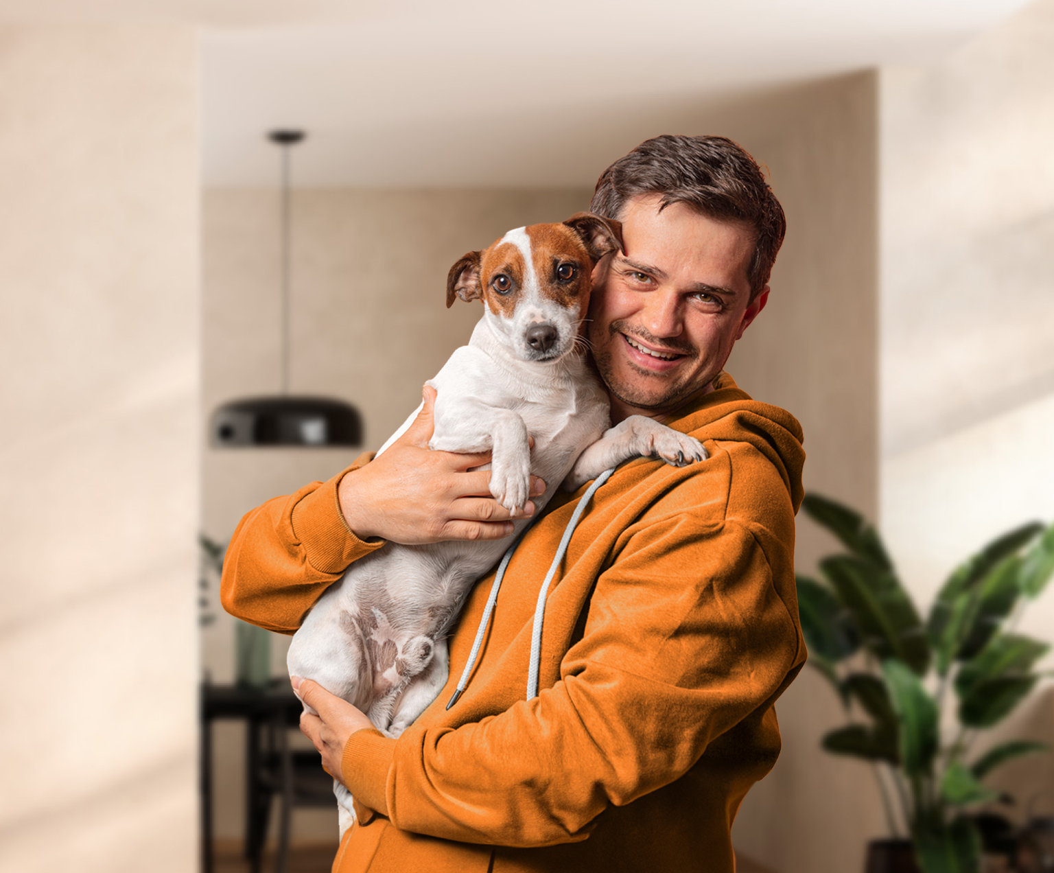 Imagem de um homem, adulto, por volta dos 30 anos, sorrindo. Ele carrega seu cachorro de porte pequeno no colo.