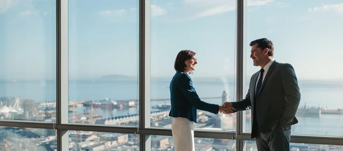 Dois executivos apertam as mãos em um escritório de vidro com vista urbana, simbolizando a parceria B2B da CNP Seguradora